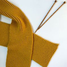 an orange knitted scarf next to two knitting needles on a white surface with brown sticks sticking out of it