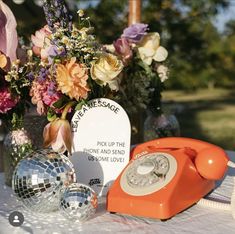 an orange phone sitting on top of a table next to a vase filled with flowers