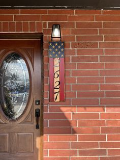 a wooden door with an american flag sign hanging on it's side and a brick wall behind it