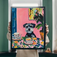 a woman holding up a painting of a dog and teacups on a table