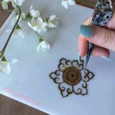 a woman's hand holding a pen over a piece of paper with flowers on it