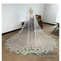 a wedding veil with white flowers on the bottom and green leaves on the bottom, sitting in front of a chair