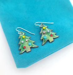 "These Christmas tree earrings are perfect to put you in the festive spirit throughout the holiday season! The earrings are cut from copper sheet, and then enameled with glass enamel in a kiln.  The trees are about 1\" from top to bottom, with solid sterling silver ear wires at the top.  Colorful 'ornaments' accent the tree design. Wear these to holiday parties or gift them to a friend, or both! Colorful ornaments decorate the trees and give them some fun life :) I will include small rubber stop Festive Green Nickel-free Earrings, Colorful Ornaments, December Birthday, Fun Life, Tree Earrings, Holiday Earrings, Christmas Tree Earrings, Copper Sheets, Earrings Christmas