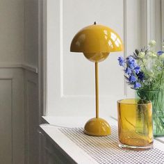 a yellow lamp sitting on top of a table next to a vase filled with flowers