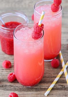 two glasses filled with raspberry lemonade on top of a wooden table next to strawberries