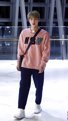 a young man wearing a pink sweater and blue pants standing in front of a building