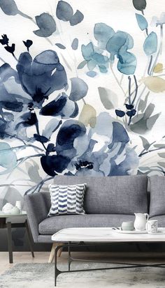 a living room with blue flowers on the wall and grey couches in front of it