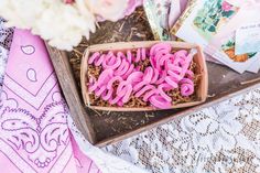 pink donuts are sitting in a box on a table next to some cards and flowers