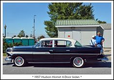 an old black and white car parked in front of a building with a man standing next to it