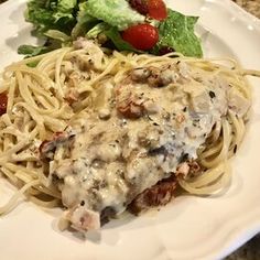 a white plate topped with pasta and meat covered in gravy next to a salad