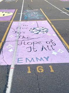 an empty parking lot with chalk writing on the ground and painted in yellow, purple, and blue