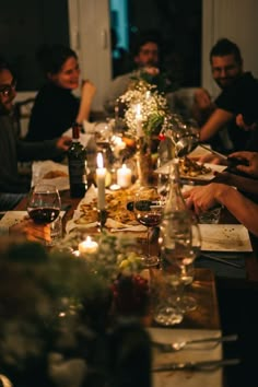 a group of people sitting around a dinner table with food and wine glasses on it