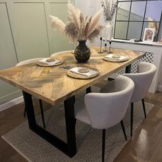 a wooden table with white chairs and a vase filled with feathers on top of it