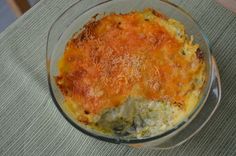 a casserole dish with cheese and spinach in a glass bowl on a table