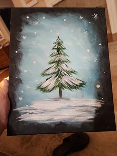 someone holding up a painting of a christmas tree in the snow with stars on it