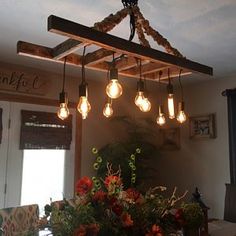 a bunch of light bulbs hanging from a wooden beam above a table with flowers on it