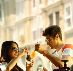 a man and woman sitting at a table with drinks in front of them, eating