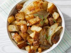 a white bowl filled with cooked potatoes on top of a blue and white cloth next to a spoon