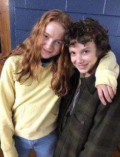 two young people standing next to each other in front of a blue wall and smiling