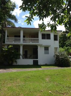 a large white house sitting in the middle of a lush green field with lots of trees