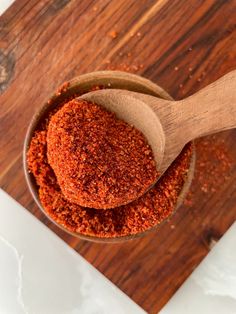 a wooden spoon filled with red seasoning on top of a cutting board