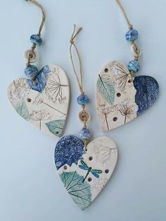 three heart shaped ceramic ornaments hanging from strings on a white surface with blue flowers and leaves