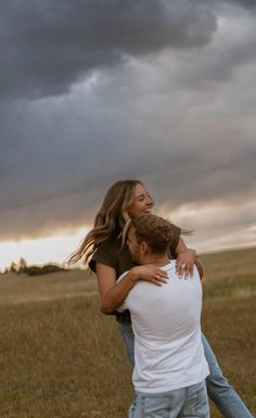 a man and woman hugging in the middle of a field under a dark cloudy sky