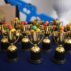 there are many gold cups with candies on top of each one in front of a blue table cloth