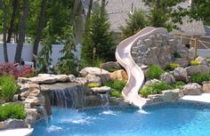 a water slide in the middle of a pool surrounded by rocks and plants with a waterfall running down it