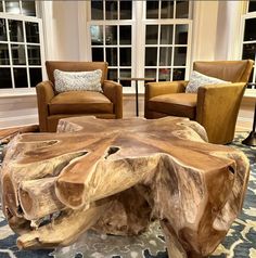 a living room with two chairs and a table made out of tree trunks in front of windows