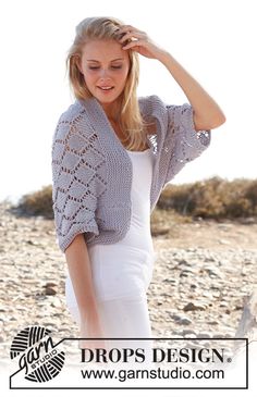 a woman standing on top of a rocky beach wearing a white dress and cardigan