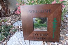 a wooden sign that says welcome to our cabin on the side of a rock garden