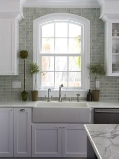 a kitchen with white cabinets and marble counter tops, along with a window over the sink