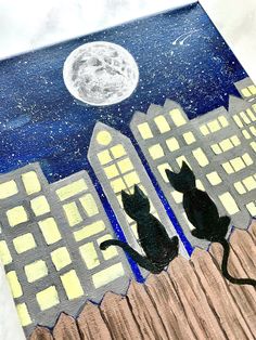 two black cats sitting on top of a fence in front of a city at night