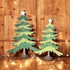 two wooden christmas trees with lights around them on a wood floor in front of a wall