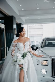 a woman standing next to a white car wearing a wedding dress and holding a bouquet