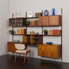 a wooden shelf with books, vases and other items on it next to a chair