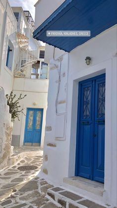 an alleyway with blue doors and steps leading up to the second floor, in front of a white building