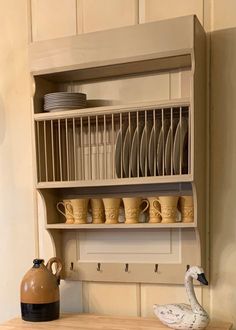 a shelf with plates and cups on it next to a tea kettle, mugs and a goose