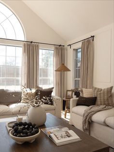 a living room filled with furniture and a large window covered in drapes, next to a coffee table