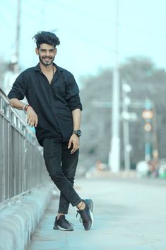 a man leaning against a fence with his foot on the rail and smiling at the camera