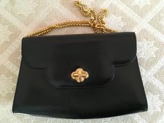 "This handsome bag by Bally is made of black leather, inside and out. It closes with a gold tone toggle clasp on the front flap. Inside, there is one zippered pocket and a fancy, adjustable gold tone chain. The bag is stamped, \"Bally,\" on the front clasp and on a gold tone tag inside. There is also a cloth tag attached that says, \"Bally, Made in Italy.\" Materials: Leather Gold tone hardware Measurements: Length - 10\" Height - 7\" Handle drop - 17\" Width - 2 1/2\" There is light wear on the exterior consistent with vintage. Otherwise, this bag is in very good, used condition." Luxury Bags With Gold Clasp For Formal Occasions, Classic Formal Bag With Gold Clasp, Classic Formal Bags With Gold Clasp, Formal Leather Bag With Gold Clasp, Leather Evening Bag With Gold Clasp, Evening Leather Bag With Gold Clasp, Classic Formal Shoulder Bag With Gold Chain, Luxury Formal Shoulder Bag With Gold Chain, Vintage Gold Shoulder Bag For Business