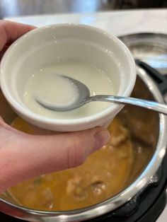 a hand holding a spoon over a bowl filled with liquid on top of a stove