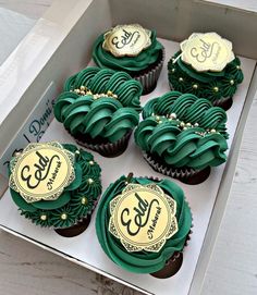 cupcakes with green frosting and gold decorations in a box on a table