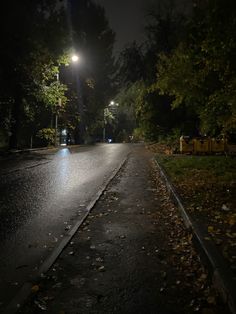 an empty street at night with the lights on and fallen leaves all over the road