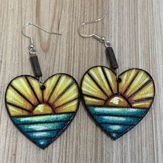 two heart shaped earrings with sunsets painted on the inside and outside, hanging from metal earwires