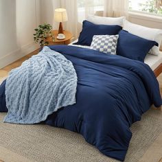 a bed with blue comforter and pillows on top of it in a room next to a window