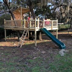 a tree house with a green slide in the grass next to a large oak tree