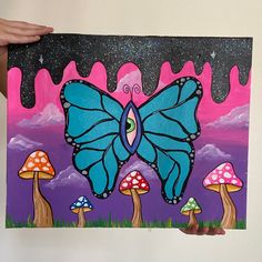 a person holding up a painting with mushrooms and a blue butterfly on it's wings