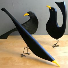 two black birds with yellow beaks sitting on top of a wooden table next to each other